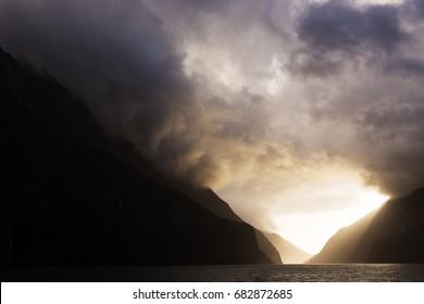 Bright sun light streams through ominous storm clouds as they hang over majestic snow capped peaks, lighting a layered path through the mountains. - Powered by Shutterstock