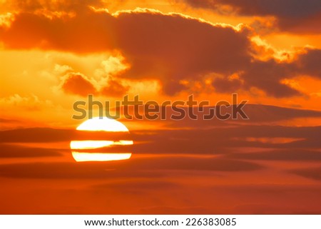 bright sun in an orange sky with dark clouds at sunset
