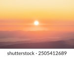 Bright sun rising over hazy mountain ranges, casting warm yellow and orange light across the landscape, creating a soft and a serene morning atmosphere . 