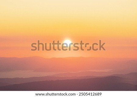 Bright sun rising over hazy mountain ranges, casting warm yellow and orange light across the landscape, creating a soft and a serene morning atmosphere . 