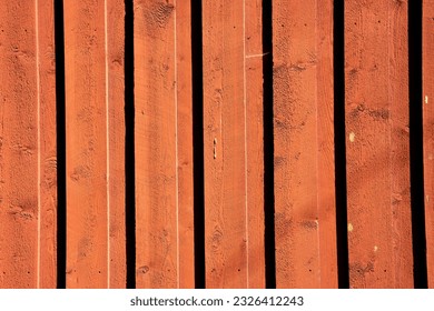 the bright sun shines on the red big wooden doors as the planks form shadow lines