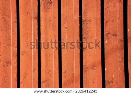 the bright sun shines on the red big wooden doors as the planks form shadow lines