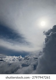 A bright sun shining over a dramatic sea of clouds and mountain peaks, creating a powerful celestial light effect.