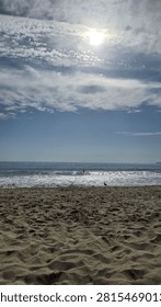 Bright sun shining through clouds over ocean waves and sandy beach