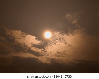 The bright sun shining through dramatic, thick clouds in a hazy or overcast sky, creating a moody atmosphere