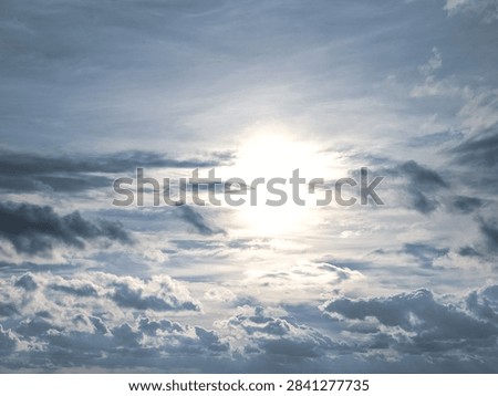 Bright sun shining through dramatic overcast sky with layered blue and gray clouds