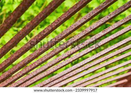 Bright sunlight reflecting silvery off red rusting metal bars with blurry green background asset