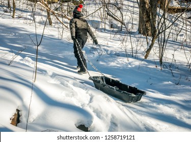 A bright and sunny mid-afternoon, casts long winter shadows, as a young boy pulls and ice covered sled up a snow covered hill