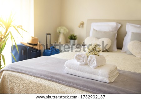 Bright and sunny vacation hotel room with suitcases and clean towel service on the bed