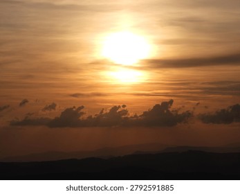 The bright sunset sun through the clouds against the backdrop of mountains