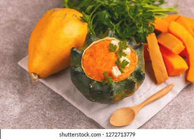 Bright tasty pureed pumpkin soup served in a hollowed pumpkin with ingredients. Healthy food concept. Gray marble background. Horizontal view. Copy space