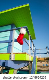 Bright Tropical Christmas Scene Of Santa Stocking Hanging From A Colorful Lifeguard Tower Under Blue Sky In Miami Beach, Florida, USA