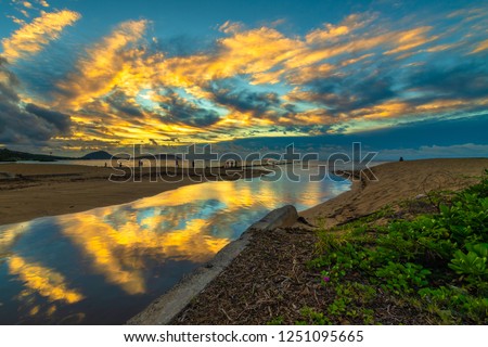 Bright tropical cloud reflections at the Waialae Beach Park in Kahala, Hawaii, at dawn - see the faint red sun rising behind the cloud cover