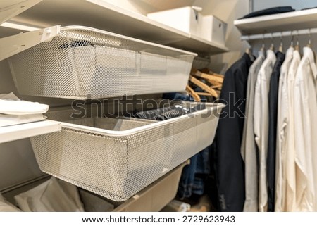 Bright wardrobe with pullout mesh baskets and clothes on hangers. Soft daytime light highlights declutter trend and capsule organization.