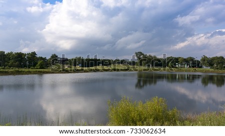Bright white fluffy clouds reflect over small mountaintop pond.