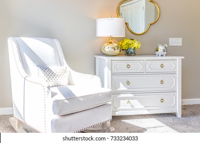 Bright white modern rocking chair in nursery room with chest of drawers, decorations in model staging home, apartment or house