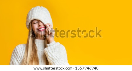 Bright winter offer, deal. Carefree blonde girl covering one eye with white knitted hat, copy space