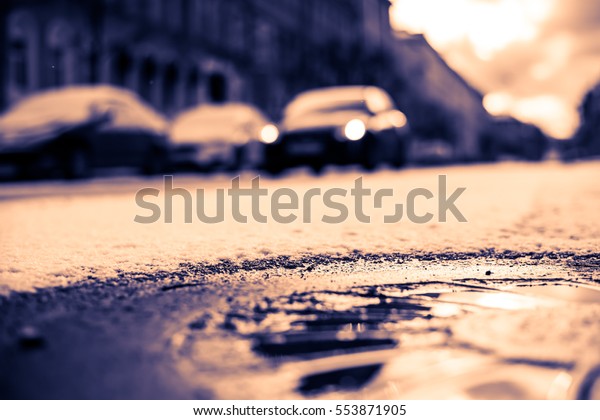 Bright winter sun in a big city, the\
headlights of the approaching car. Close up view of a hatch at the\
level of the asphalt, image in the orange-blue\
toning