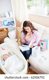 Bright Woman Sitting On The Sofa With Bags Reading A Card While Her Baby Is Sleeping In His Cradle At Home