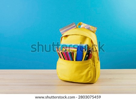 Bright yellow backpack filled with school supplies, including colored pencils and notebooks, on a wooden table.