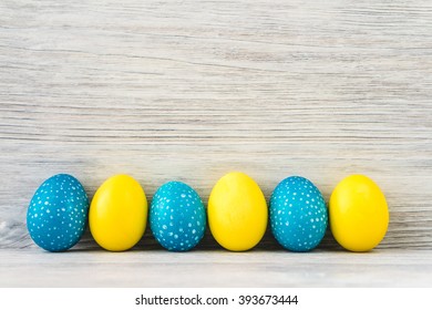 Bright Yellow And Blue Easter Eggs On White Wooden Background. Copy Space.