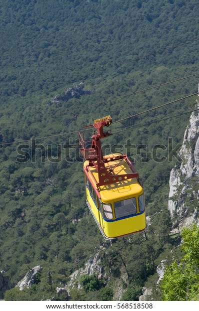 Bright yellow cable\
railway carriage hangs over the precipice. Place - Crimea. Route\
Alupka - Ai-Petri.