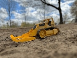 Bright Yellow Digger Toy With Focus On Sand In The Middle Range To Give A Real-world Feel To This Toy. Blue Stirs Abound With Tree Silhouettes In The Background.