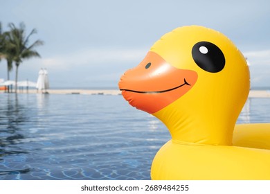 Bright yellow inflatable duck float in a swimming pool with beach background, perfect for summer vacation, travel blogs, pool party promotions, and fun holiday concepts.