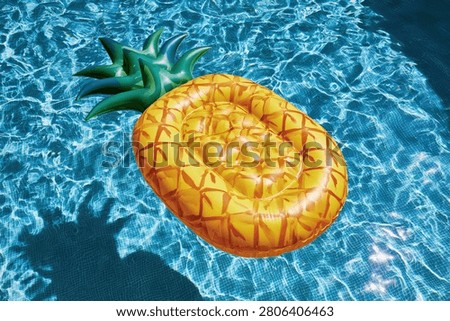 A bright yellow inflatable pineapple pool float drifts on the shimmering blue water of a swimming pool, casting a shadow.