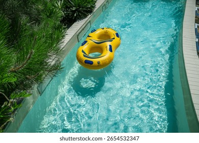 Bright yellow inflatable ring floating in a clear blue lazy river surrounded by lush greenery. A perfect summer scene symbolizing relaxation, fun, and tropical vacation vibes.
