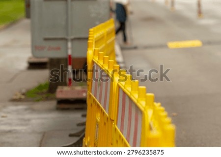 Bright yellow interlocking plastic safety barriers set up along a wet city sidewalk beside a roadway. The shallow depth of field emphasizes the repeating