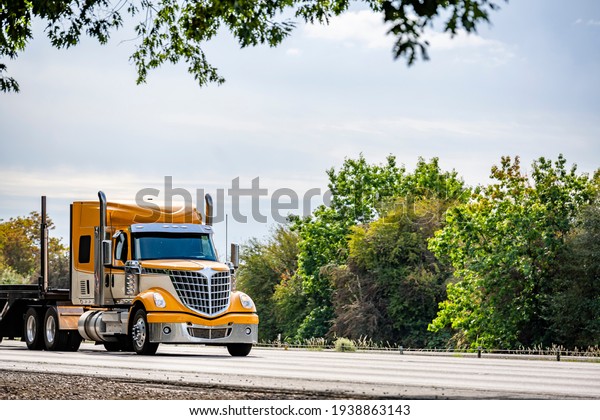 Bright yellow long hauler big rig red industrial
semi truck transporting empty step down semi trailer running on the
straight highway road with green trees on the side to warehouse for
next load