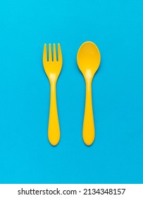 Bright yellow plastic spoon and fork on a blue background. Plastic food set. Flat lay.