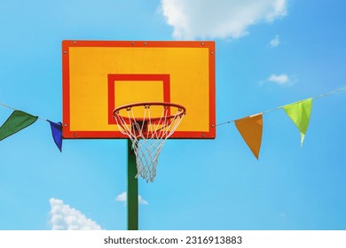 Bright yellow and red colored basketball backboard against blue sky outdoor. Basket metal hoop for basketball game competition at city street.