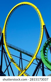 A bright yellow roller coaster loop stands out against a clear blue sky, intersecting with black supports and a green track piece.