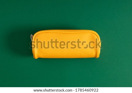 Bright yellow school pencil case, accessories on green background. Back to school. Flat lay, top view, copy space