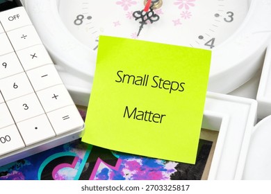 A bright yellow sticky note emphasizes the phrase Small Steps Matter placed next to a clock and calculator, symbolizing the value of taking gradual steps in lifes journey.