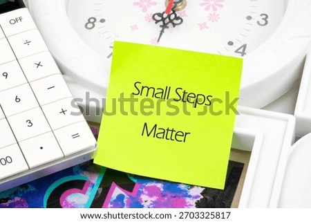 A bright yellow sticky note emphasizes the phrase Small Steps Matter placed next to a clock and calculator, symbolizing the value of taking gradual steps in lifes journey.