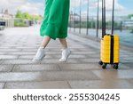 Bright yellow suitcase and woman in green dress enjoying a sunny day at a travel destination