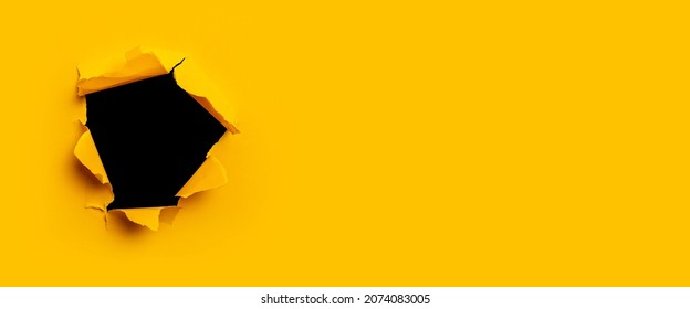 Bright yellow torn paper inside a black hole in a hole. Banner - Shutterstock ID 2074083005