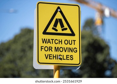 A bright yellow warning sign with a triangular caution symbol, depicting stylized pedestrian legs, and the message 