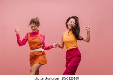 Bright young females of different nationalities dance and jump holding hands with copy space. Professional shot of two best friends having fun and laughing out loud. Leisure and lifestyle concept