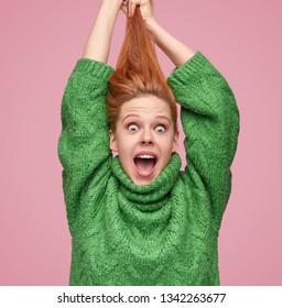 Bright Young Redhead Girl In Green Sweater Pulling Hair Up And Looking Amazed At Camera