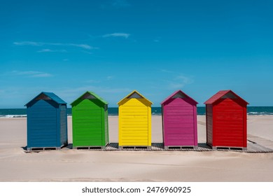 Brightly colored beach huts aligned on the sandy shore with the ocean in the background. Sant Antoni beach, Cullera, Spain - Powered by Shutterstock