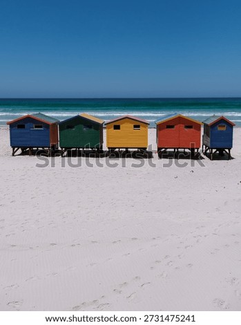 Brightly colored beach huts create a striking scene at Muizenberg beach, welcoming tourists to enjoy sun, sand, and surf in Cape Town, South Africa. A perfect escape for holidaymakers year-round.