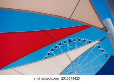 Brightly colored canopies frame the Ferris wheel in the distance, creating a playful contrast against the clear blue sky on a sunny day at the beach. - Powered by Shutterstock