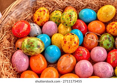 Brightly colored ceramic Easter eggs with speckled patterns lie together in a straw-filled basket, creating a cheerful spring and holiday decoration.