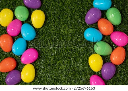 Brightly colored easter eggs creating a border on artificial green grass with copy space in centre
