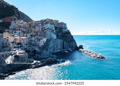 Brightly colored houses cling to the cliffs of Cinque Terre, overlooking sparkling blue waters and rocky shores. Visitors explore the charming village, Manarola in Cinque Terre Italy - Powered by Shutterstock