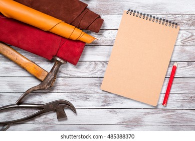 Brightly colored leather in rolls, working tools, shoe lasts, notebook with pencil on white wooden background. Leather craft.